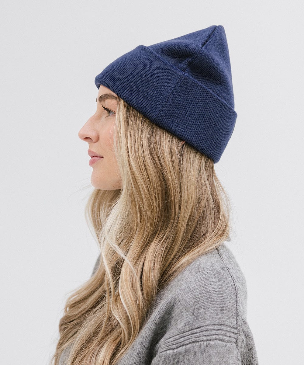 Woman wearing a navy beanie and a grey sweater, facing sideways against a plain background #color_navy