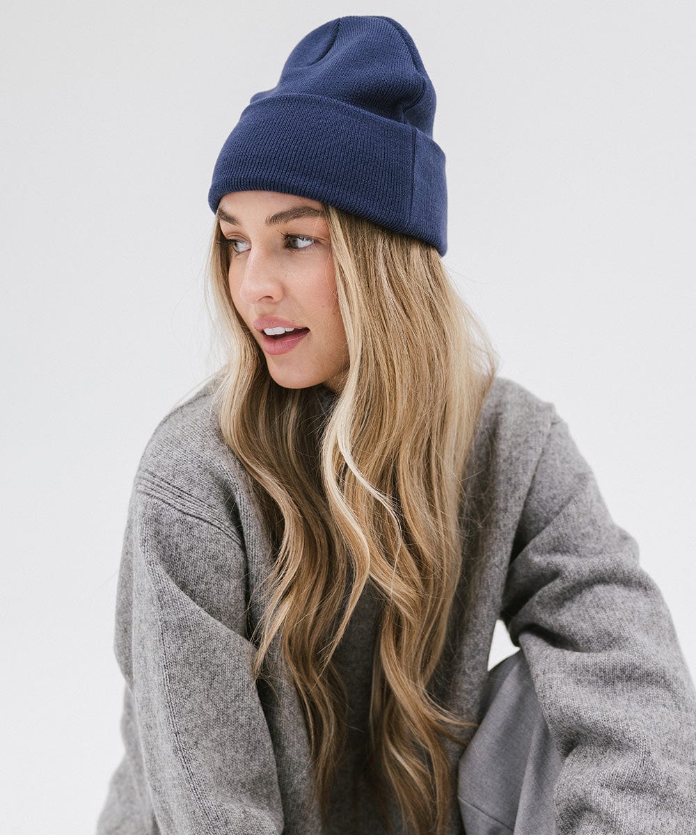 Woman wearing a navy beanie and a grey sweater, posing sideways against a plain background #color_navy