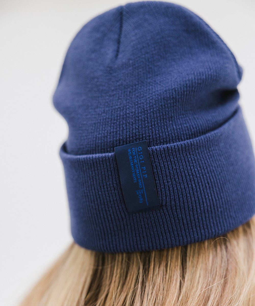 Close up image of someone wearing a navy beanie with the brand label against a plain background #color_navy