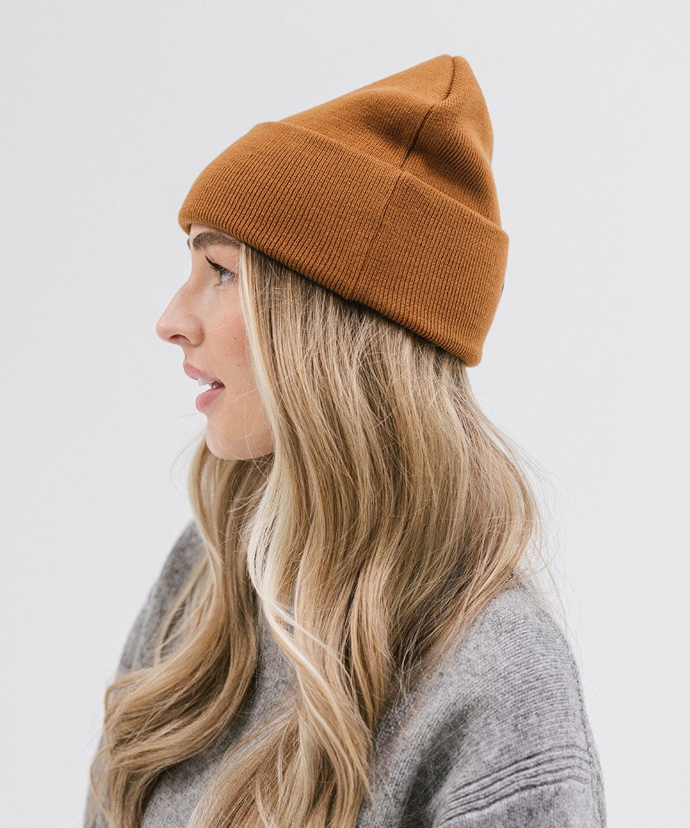 Woman wearing a cocoa colored beanie and a grey sweater, facing sideways against a plain background #color_cocoa
