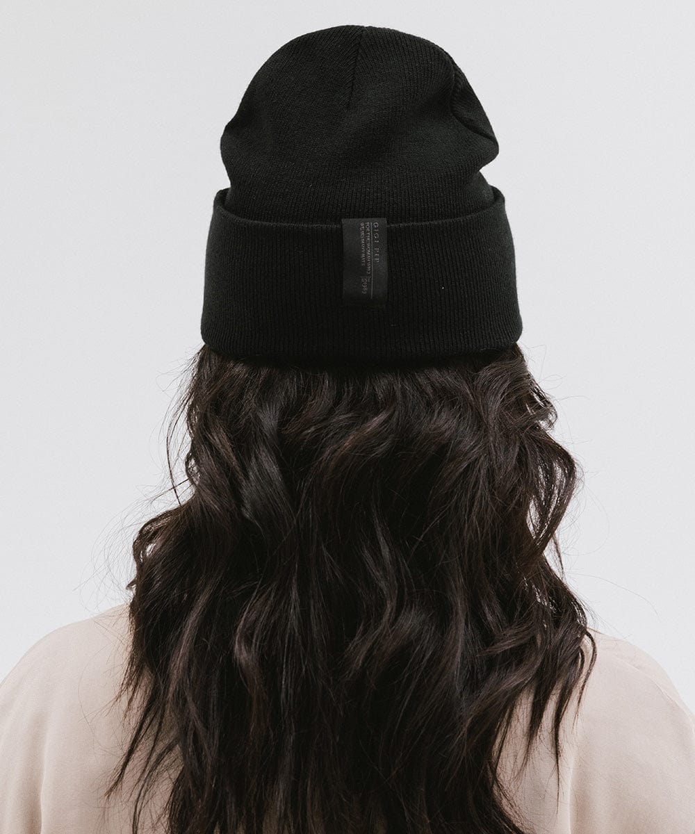 Woman with long hair wearing a black beanie and a cream shirt, facing behind against a plain background #color_black