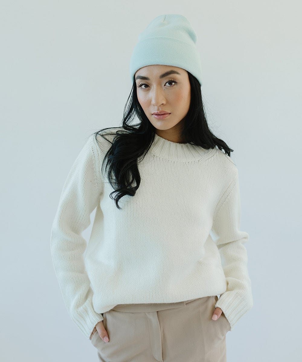 Woman wearing a sky blue beanie, a white sweater and beige pants against a plain background #color_sky blue