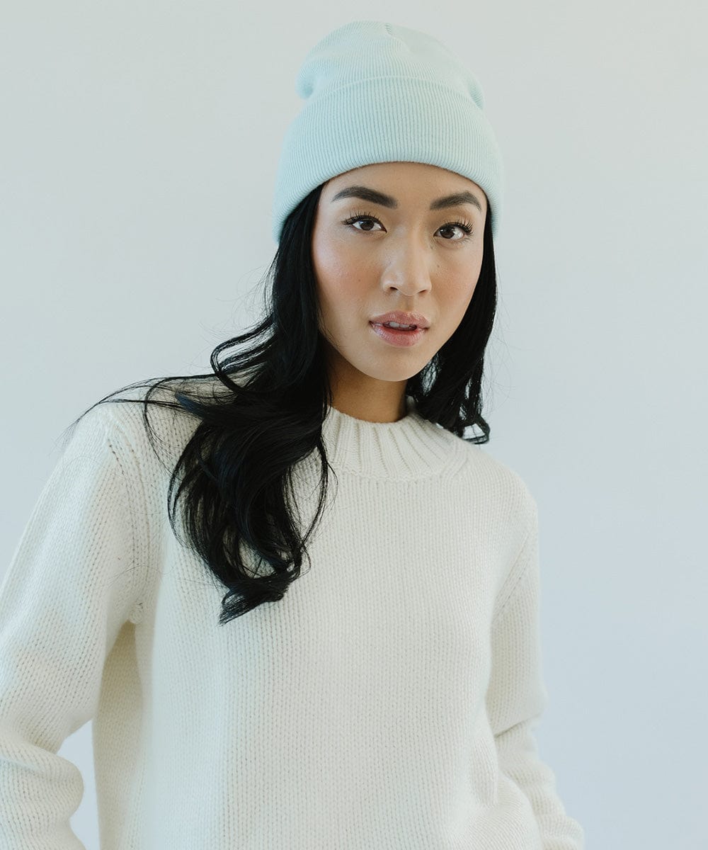 Woman wearing a sky blue beanie and a white sweater against a plain background #color_sky blue
