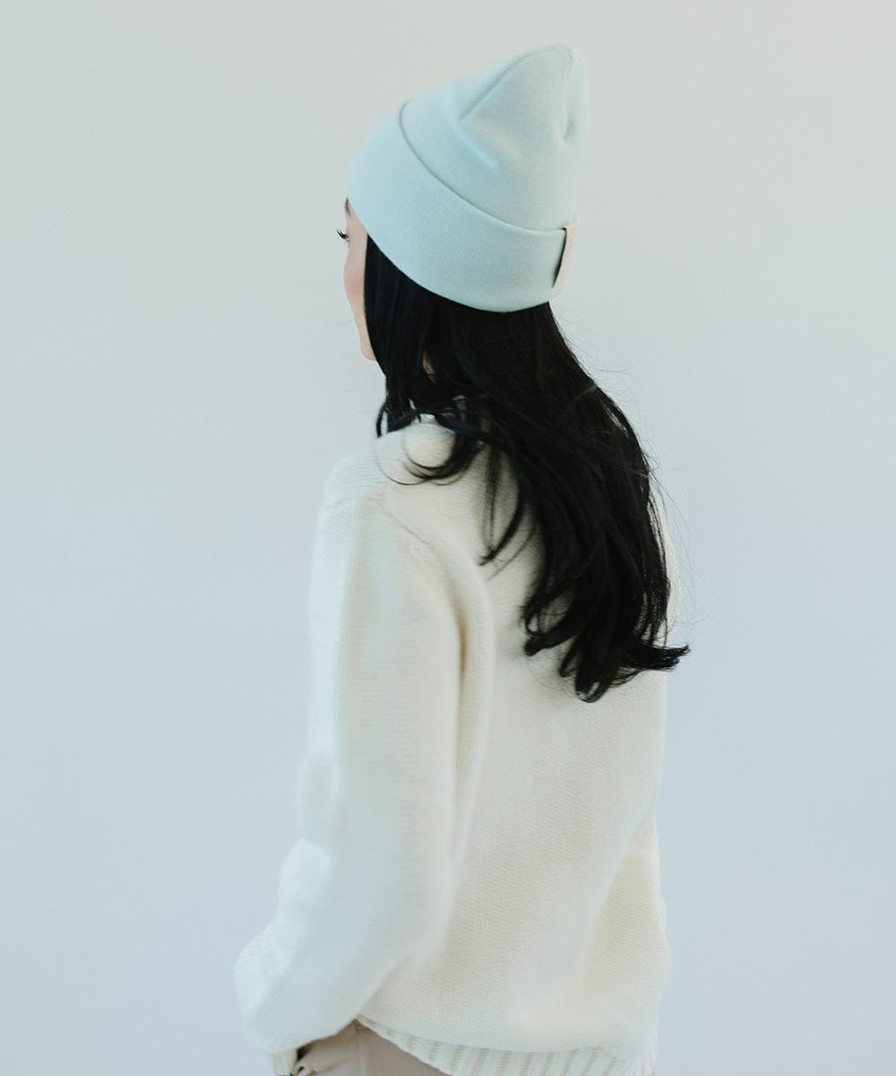 Woman with long hair wearing a sky blue beanie and a white sweater, facing behind against a plain background #color_sky blue