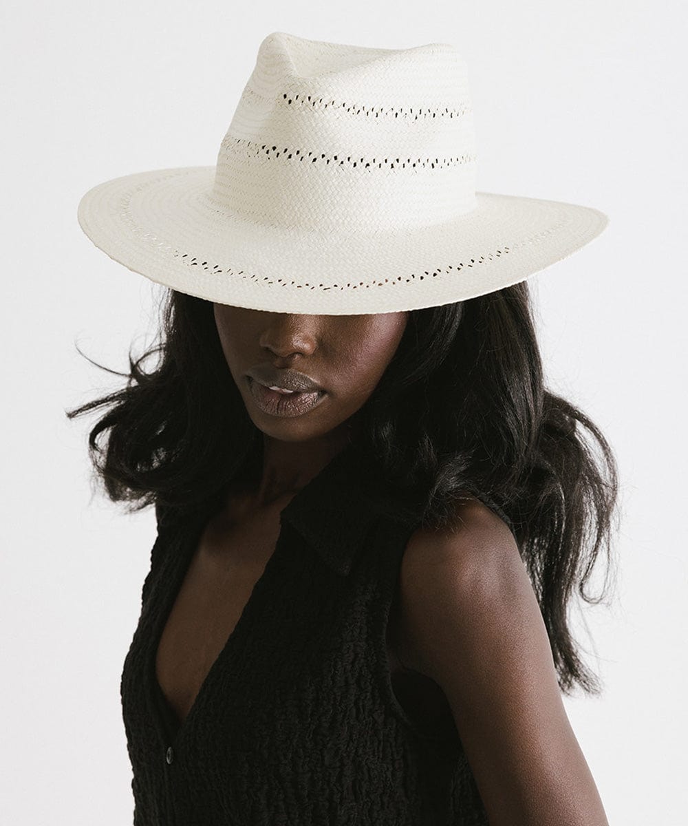 Woman wearing a white straw fedora hat with decorative trim and a black top against a plain background #color_white