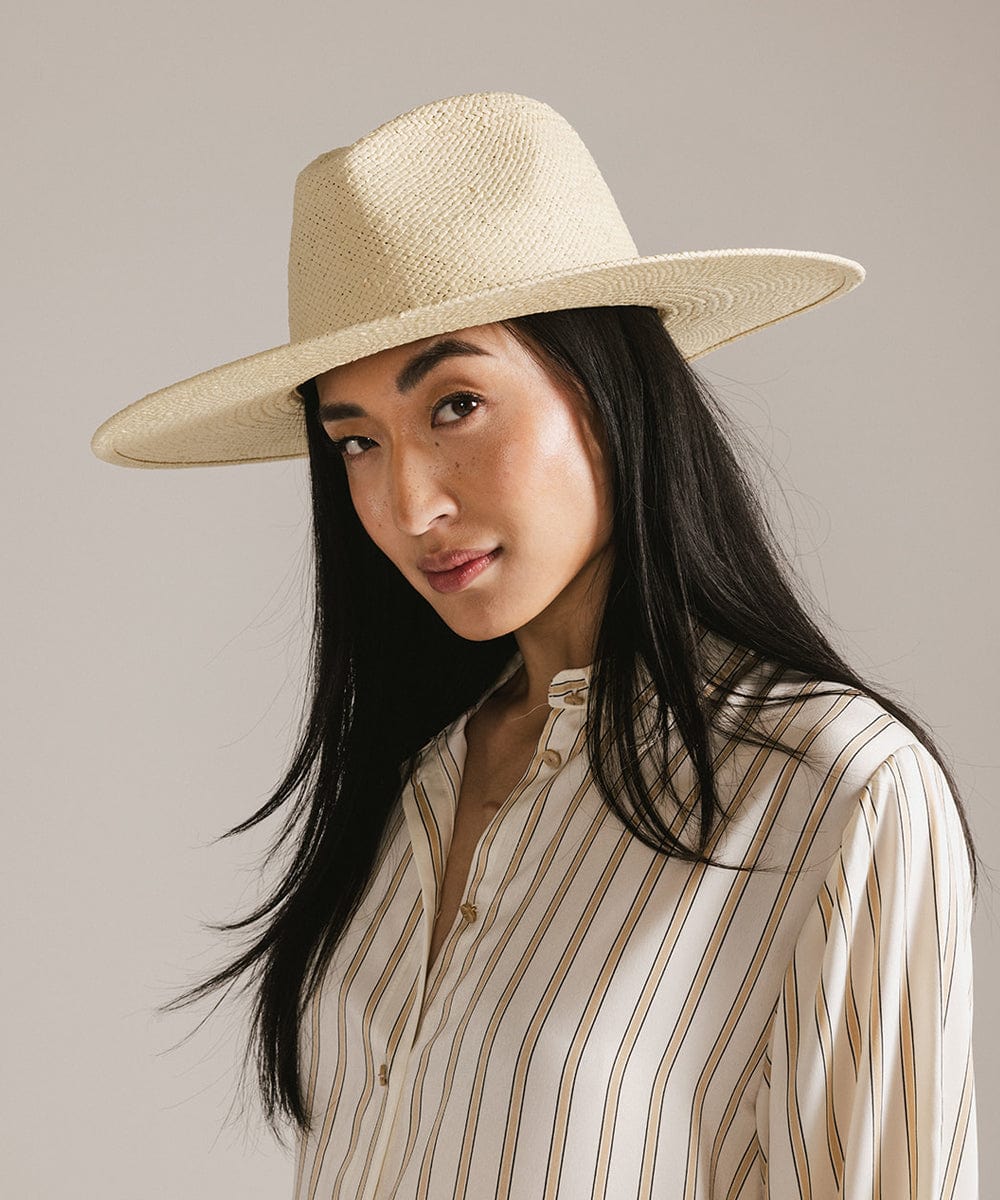 Woman wearing a natural colored wide brim fedora straw hat and a cream shirt with brown lines against a plain background #color_natural