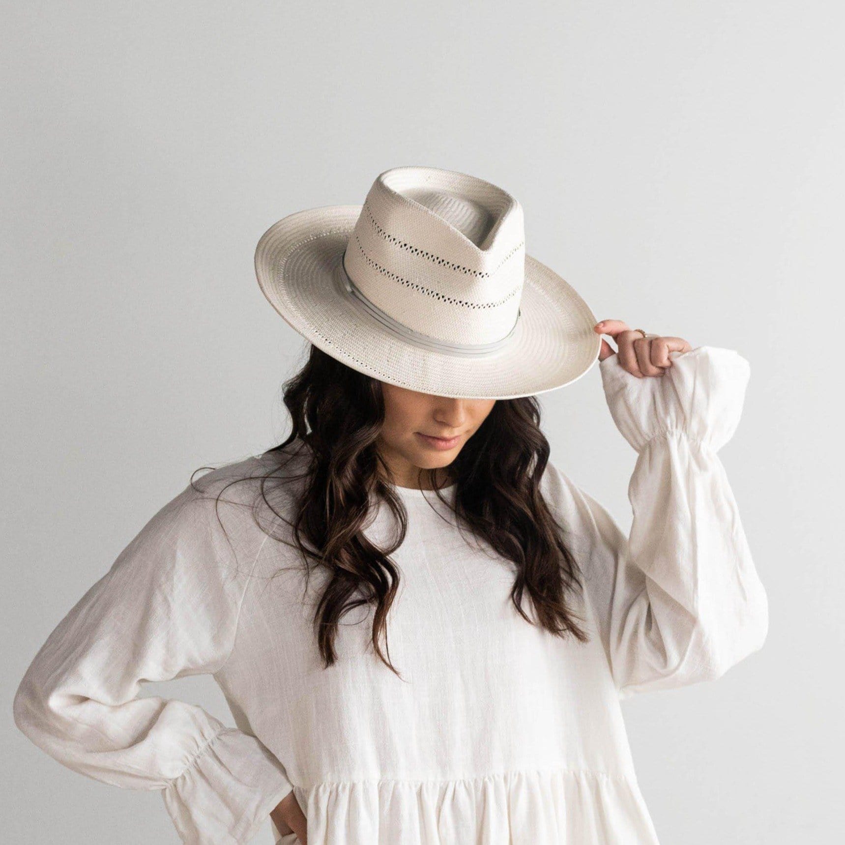 Woman wearing a grey straw fedora hat with a hat band and a white top against a plain background #color_grey