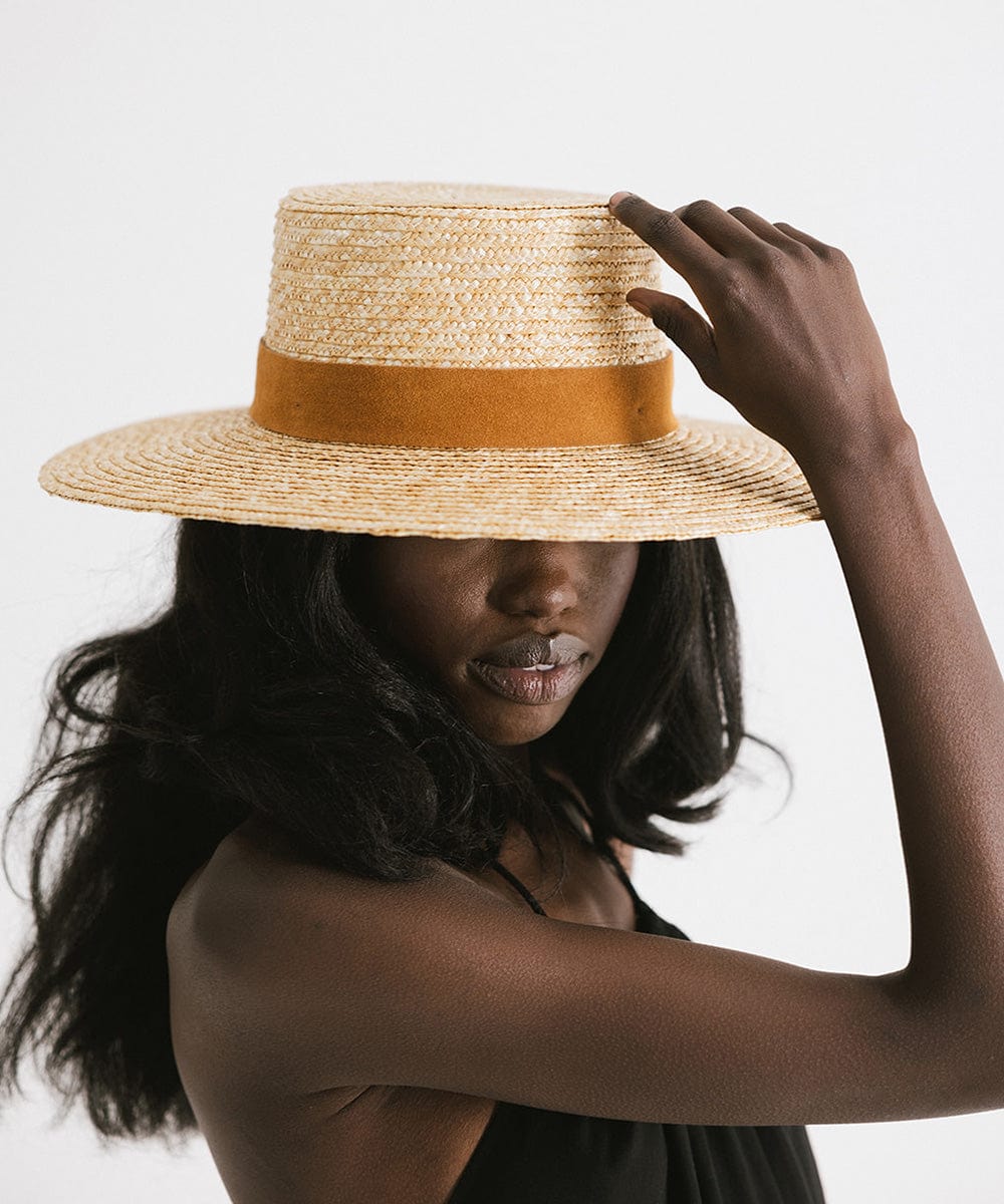 Woman wearing a natural colored straw hat with a hat band against a plain background #color_natural