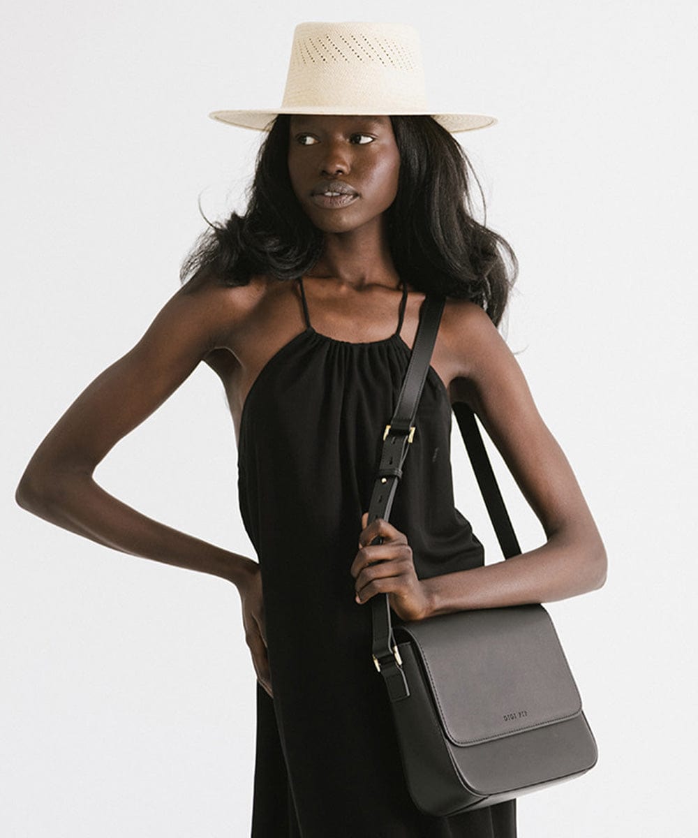Woman wearing a natural colored straw hat and a black top, carrying a black bag against a plain background #color_natural