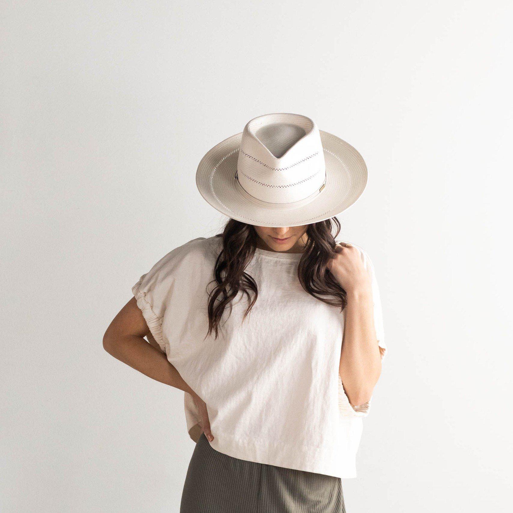 Woman wearing a cream fedora straw hat with a hat band, a white t-shirt and grey pants against a plain background #color_cream