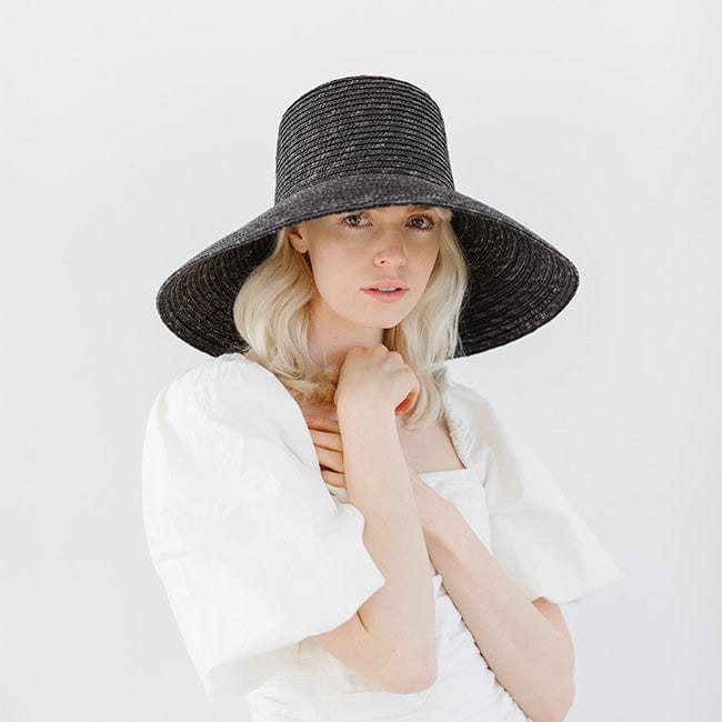 Woman wearing a black straw boater hat and a white top against a plain background #color_black
