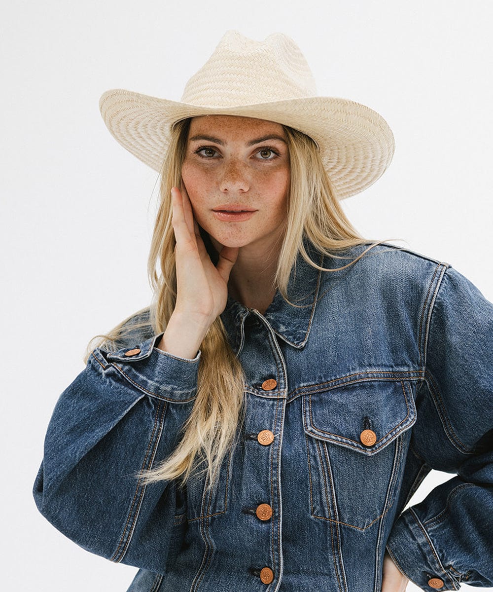 Woman wearing a natural colored straw cowboy hat and a denim shirt against a plain background #color_natural