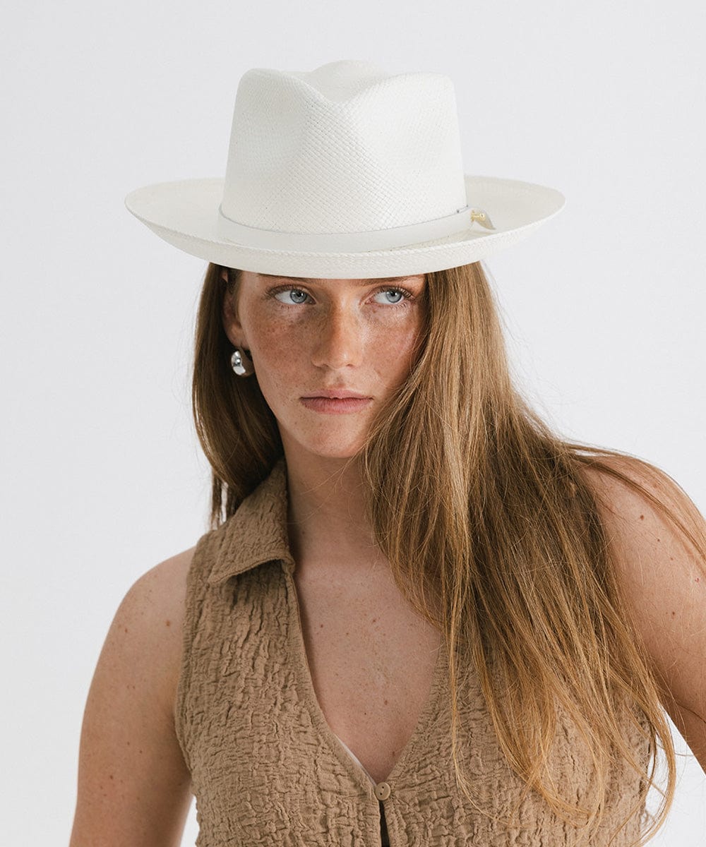 Woman wearing a white straw hat with a hat band and a brown top against a plain background #color_white