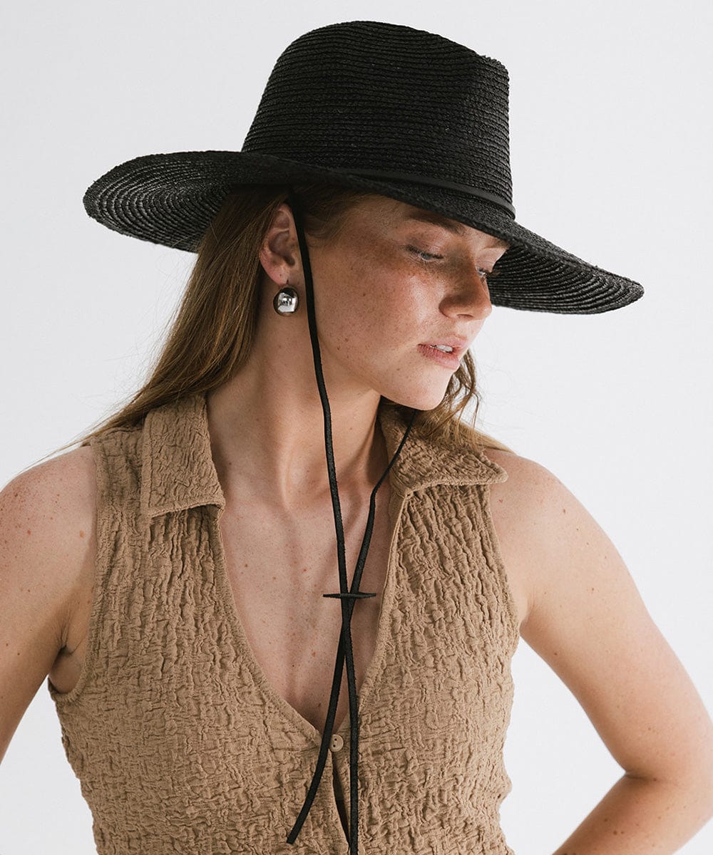 Woman wearing a black straw hat with a band and a brown top, looking sideways against a plain background #color_black