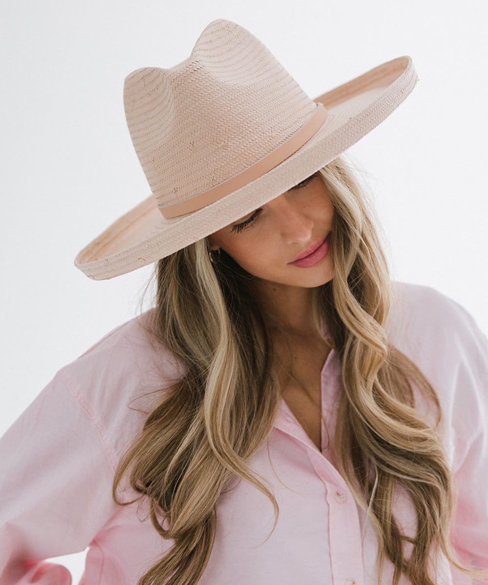 Woman wearing a light pink pencil brim straw fedora hat with a hat band and a pink shirt against a plain background #color_limited edition light pink