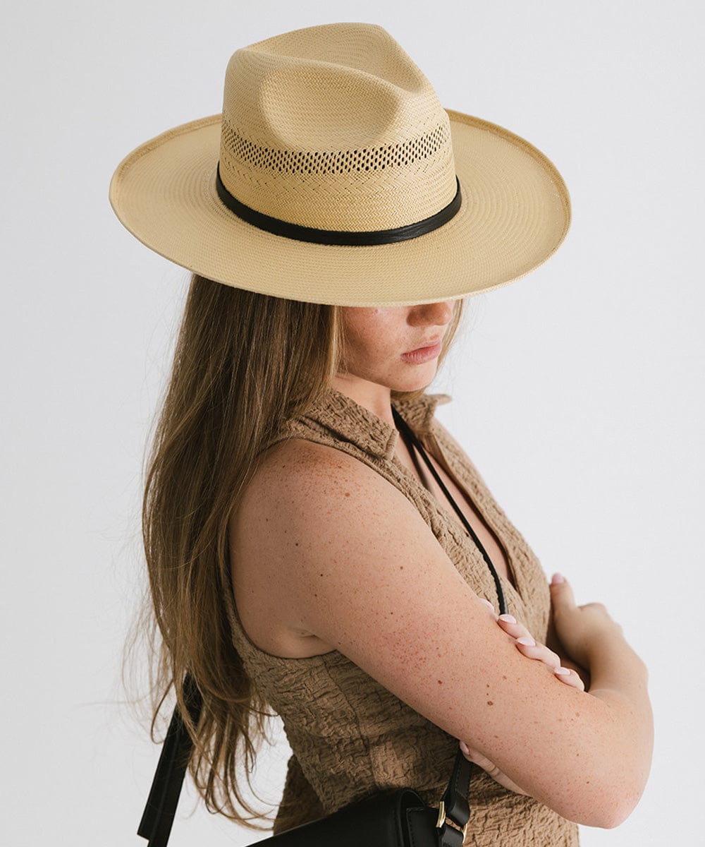 Woman wearing a natural colored straw fedora hat with a hat band and a brown top, posing sideways against a plain background #color_natural