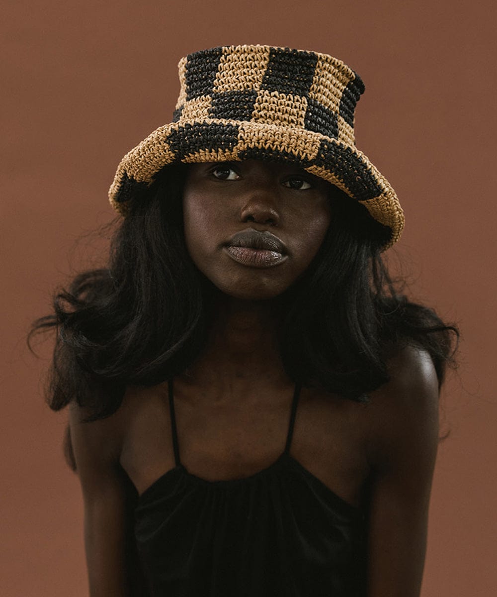 Woman wearing a black check crochet packable bucket hat and a black top against a brown background #color_black check