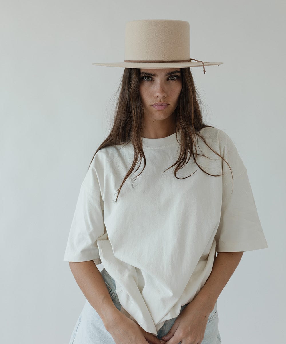 Woman wearing a beige hat with a brown suede band, a white t-shirt and light blue jeans against a plain background #color_brown