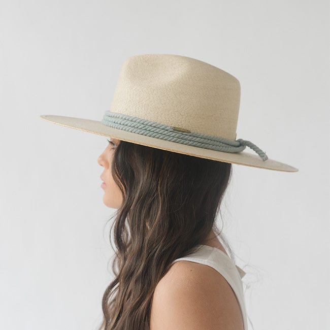 Woman wearing a beige hat with a dusty blue colored thick rope hat band and a white top, facing sideways against a plain background #color_dusty blue
