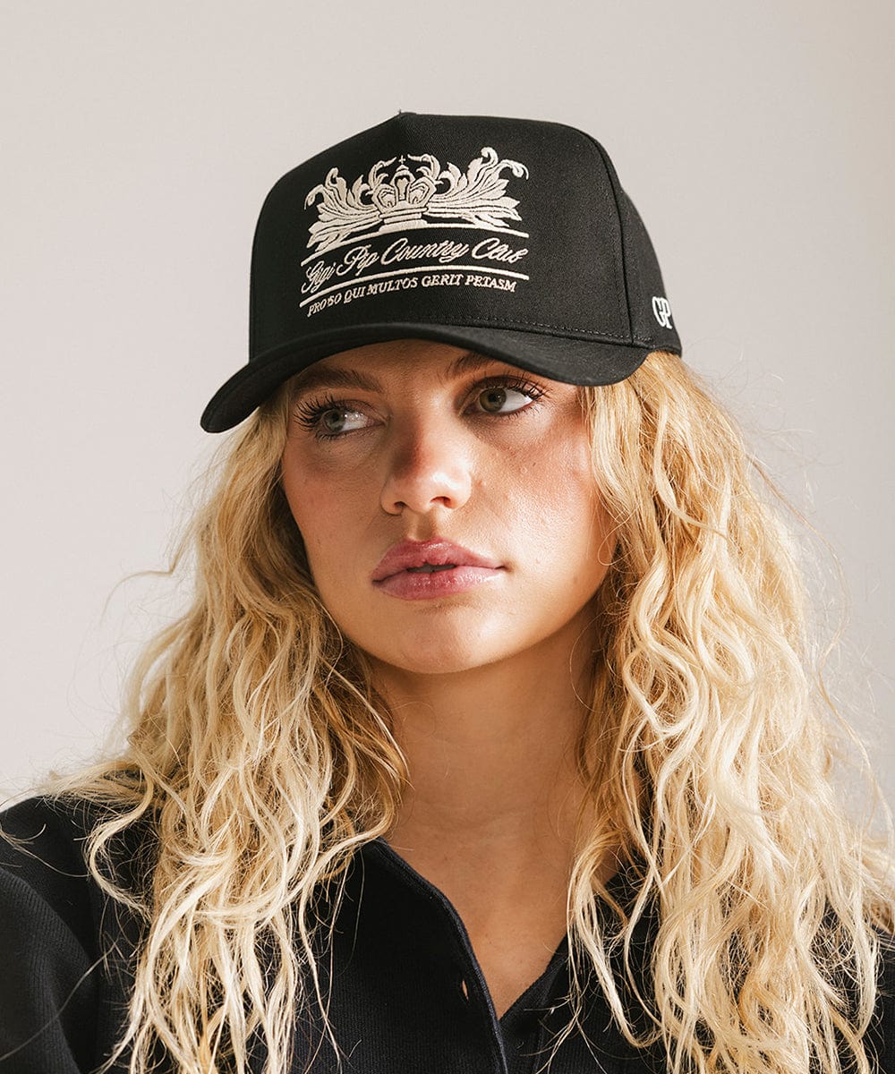 Woman wearing a black vintage trucker cap with a white logo against a plain background #color_black