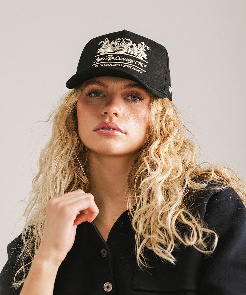 Woman wearing a black vintage trucker cap with a white logo and a black shirt against a plain background #color_black