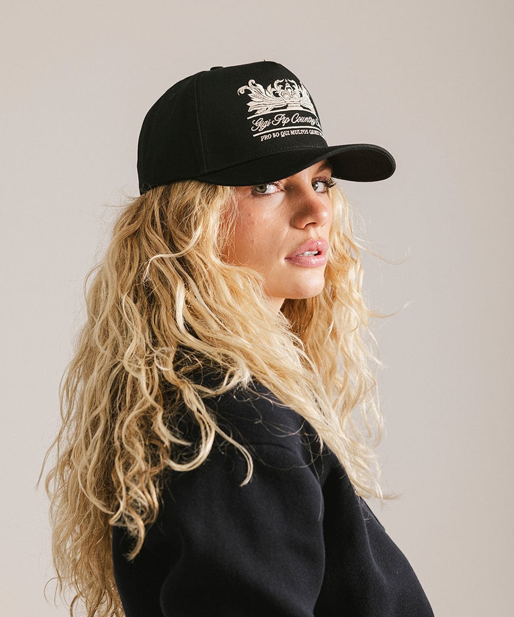 Woman wearing a black vintage trucker cap with a white logo and a black shirt, posing sideways against a plain background #color_black