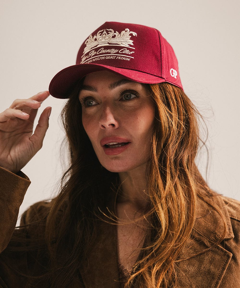 Woman wearing a burgundy vintage trucker cap with a white logo and a brown coat against a plain background #color_burgundy