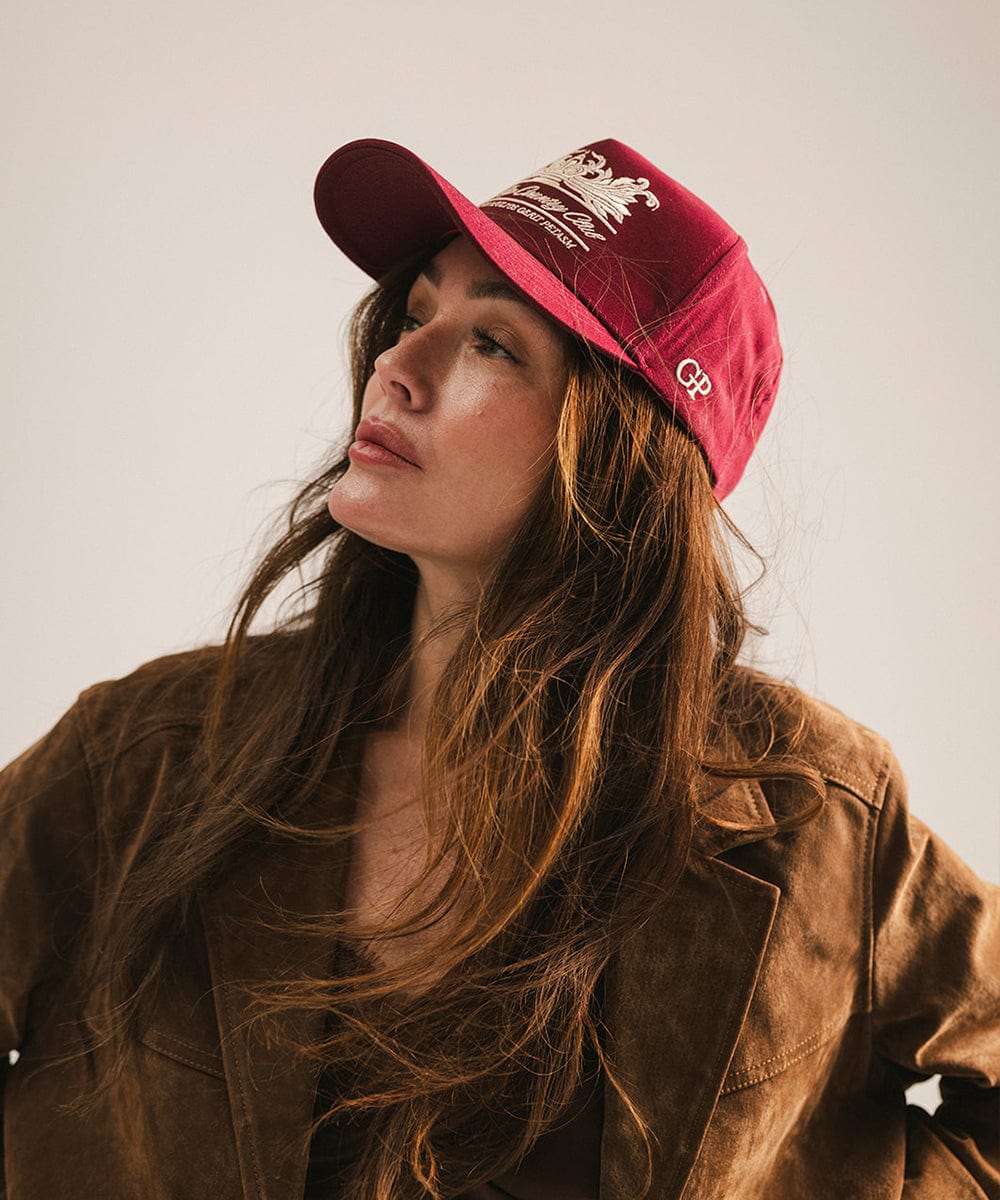 Woman wearing a burgundy vintage trucker cap with a white logo and a brown coat, posing against a plain background #color_burgundy