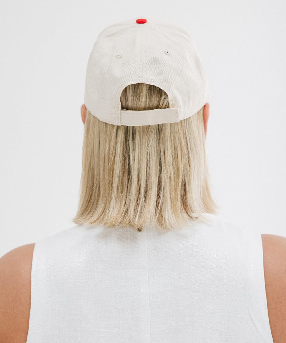Woman wearing a cream and red trucker hat and a white top against a plain background #color_cream - red