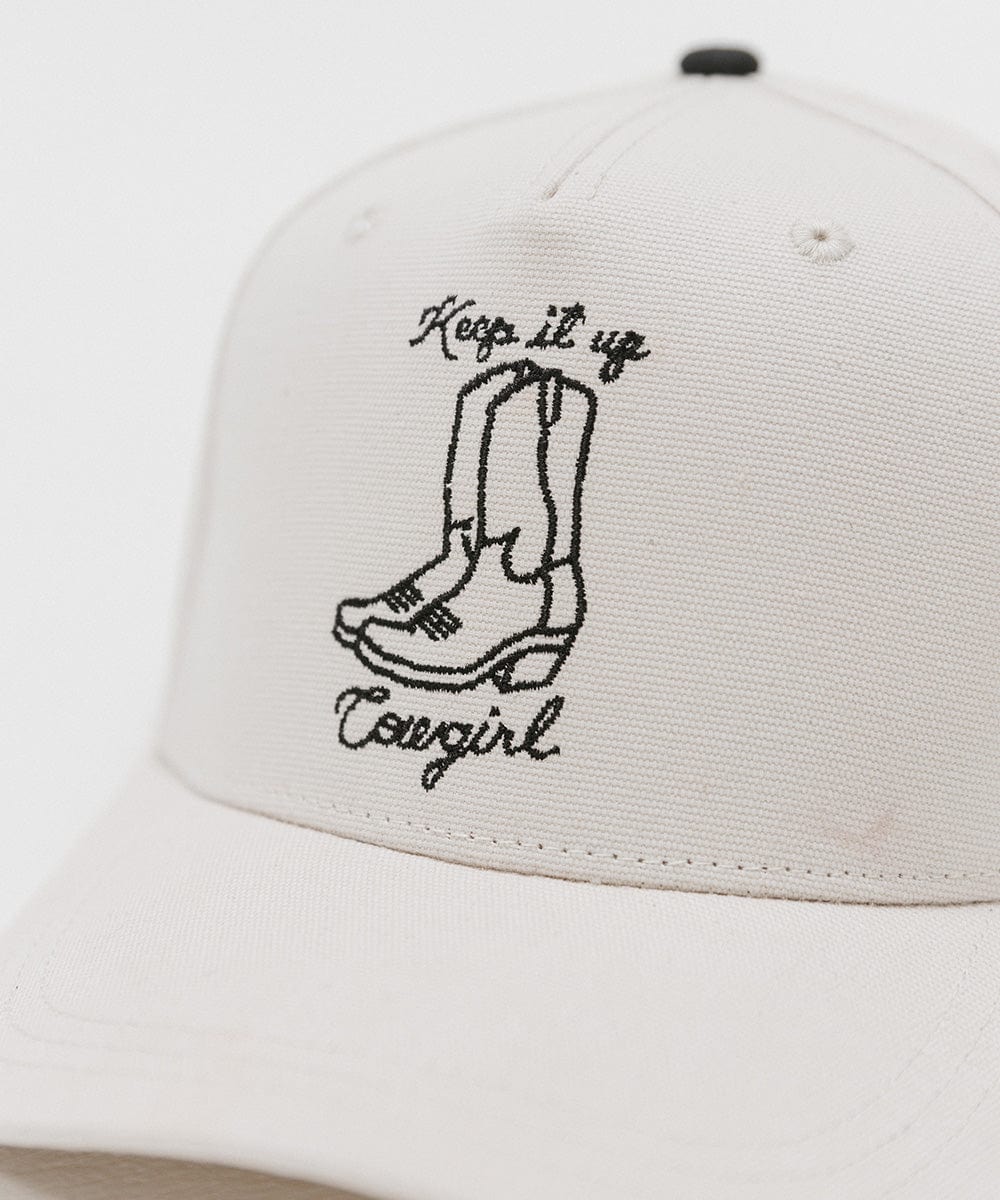 Close up image of a cream cap with black text and boot design on a white background #color_cream
