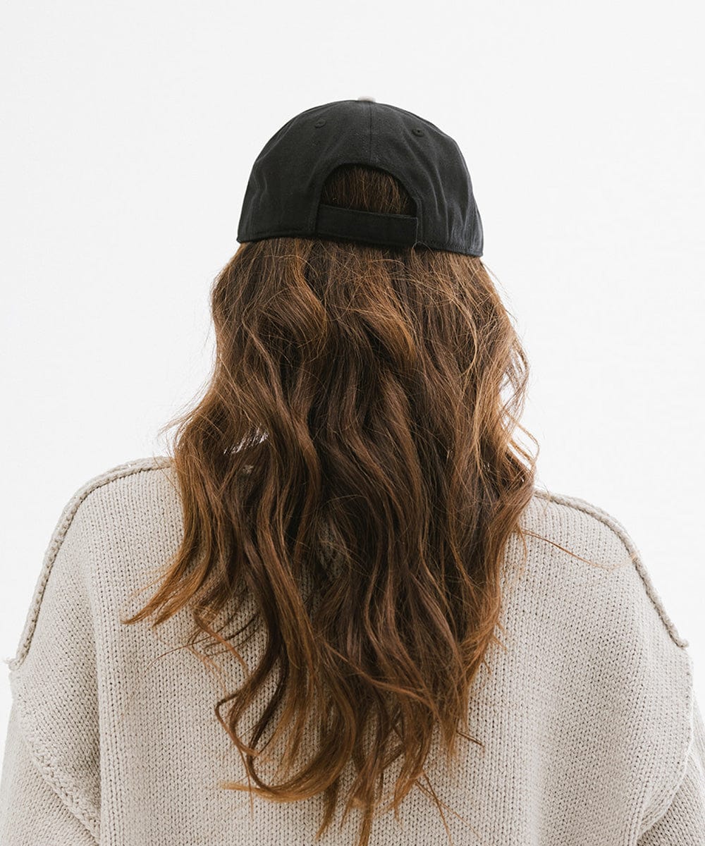 Woman with long brown hair wearing a black cap and an off white t-shirt against a plain background #color_black