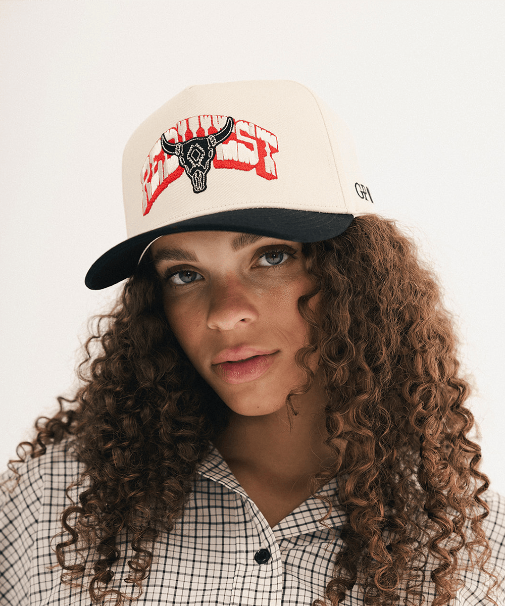 Woman wearing a beige and black cap with bull logo on a white background #color_cream - black