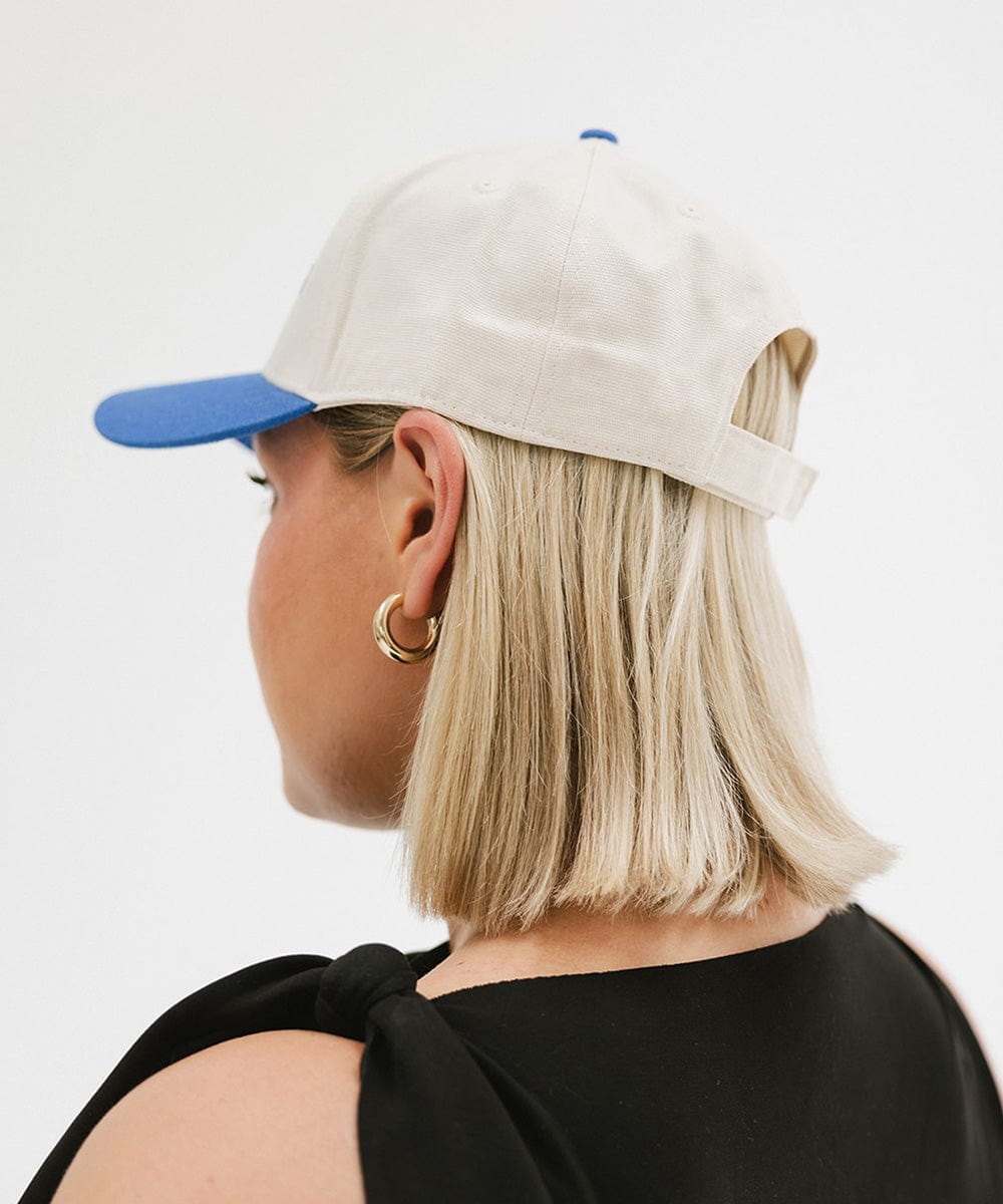 Person wearing a cream and blue cap with 'Slow Morning Club' text and a black top, facing behind against a plain background #color_cream - blue