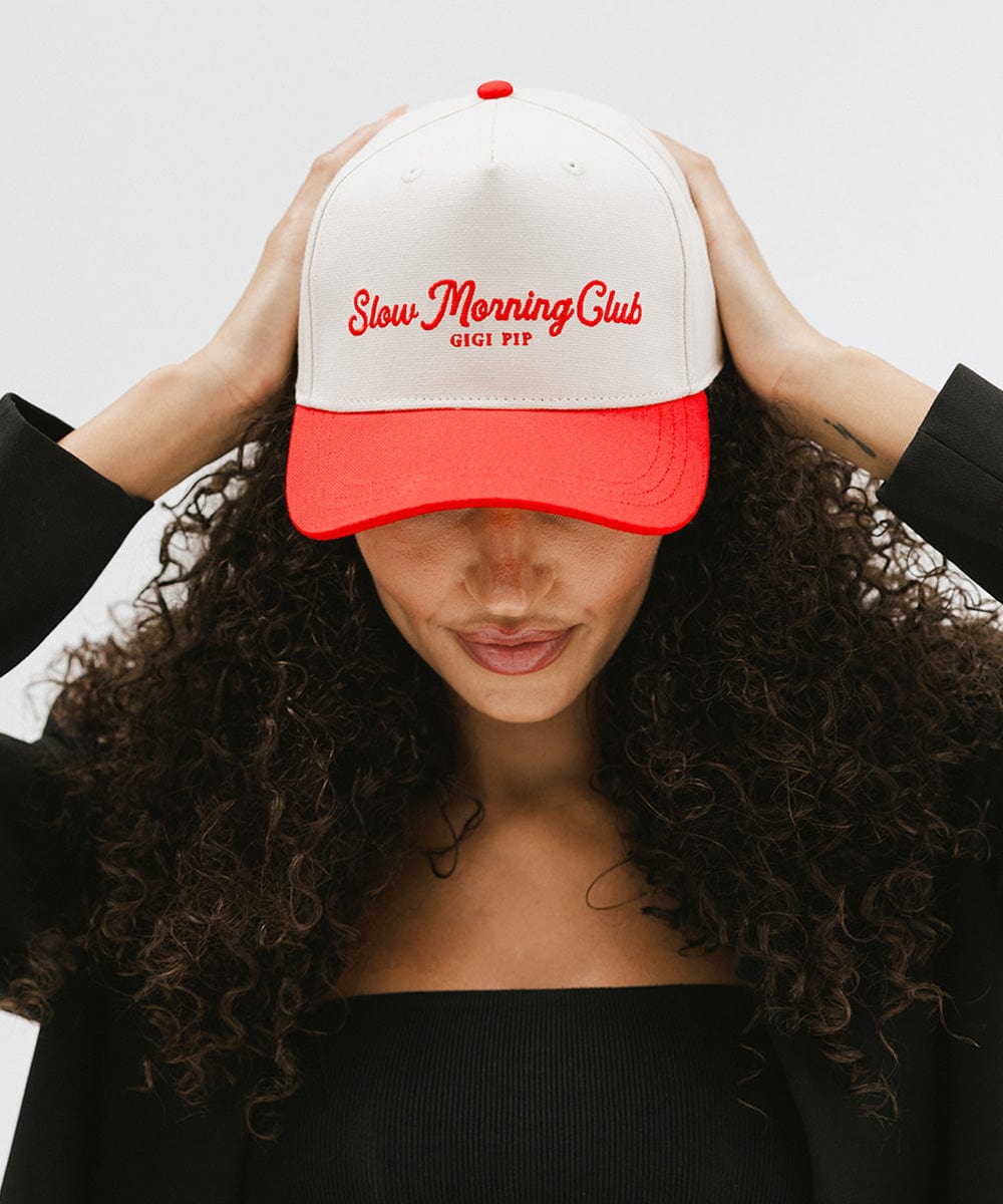 Woman wearing a cream and red cap with 'Slow Morning Club' text and a black coat against a plain background #color_cream - red