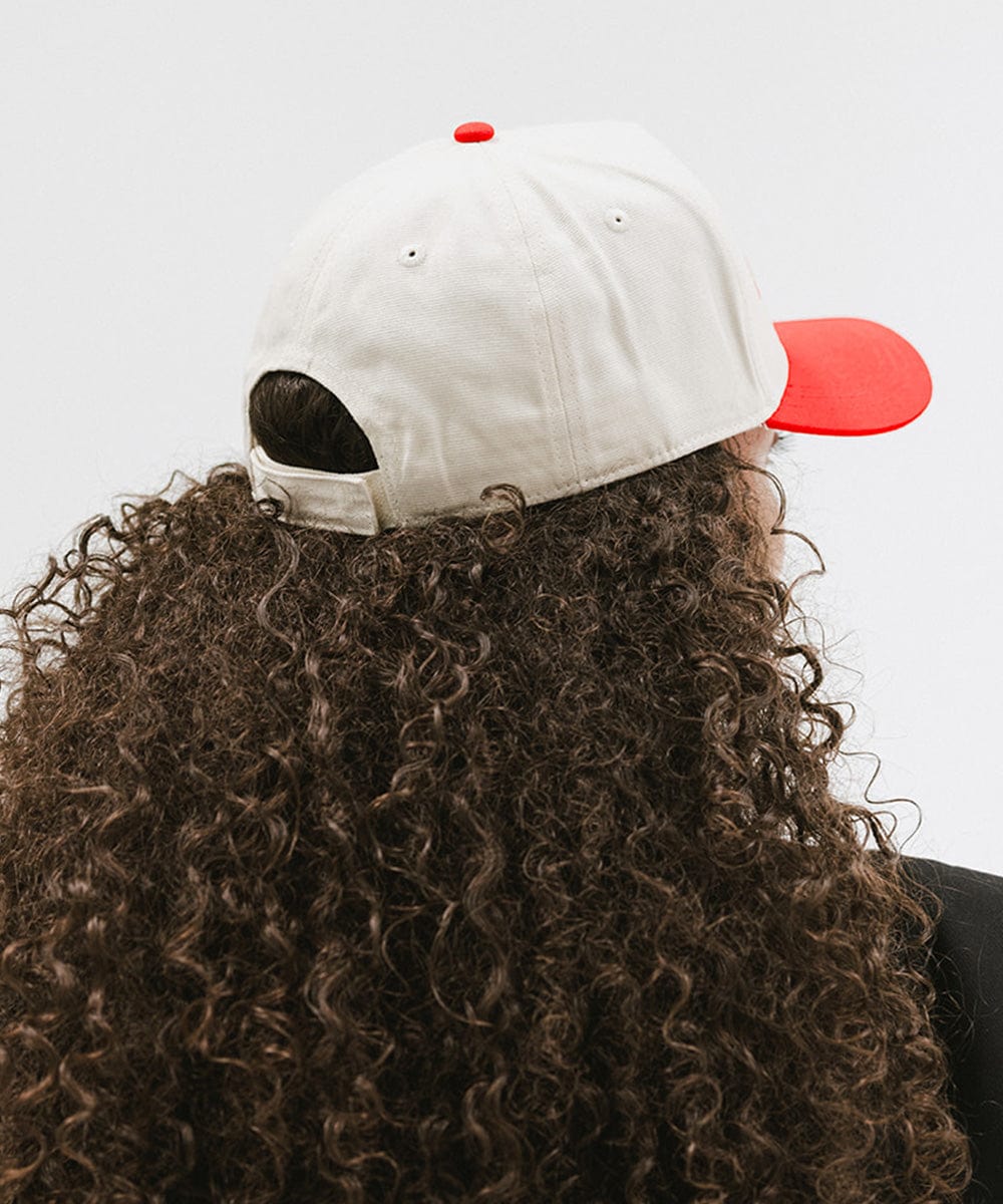 Person with curly hair wearing a cream and red cap with 'Slow Morning Club' text against a plain background #color_cream - red