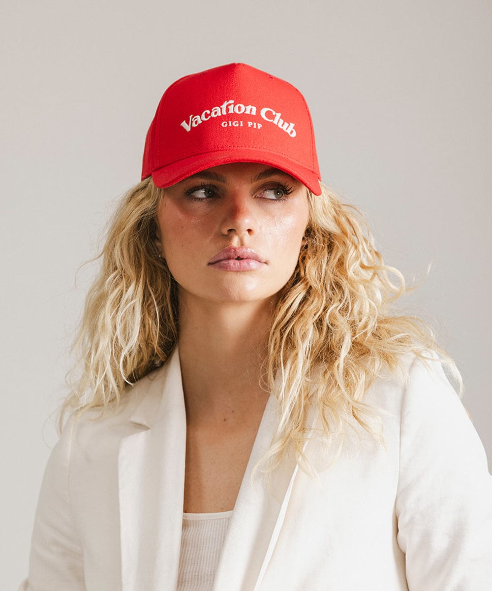 Woman wearing a red cap with 'Vacation Club' text and a white coat against a plain background #color_red