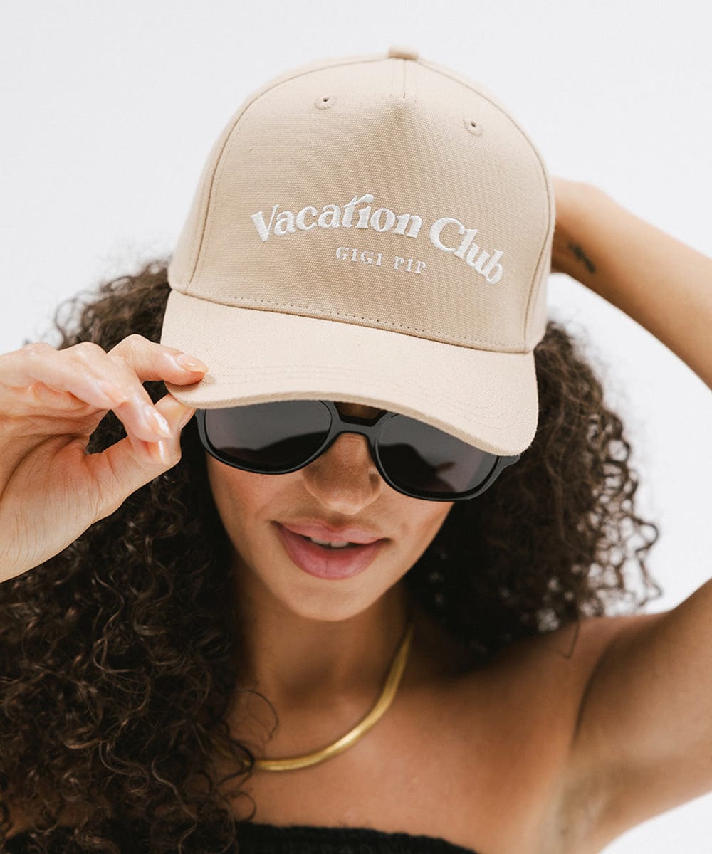 Woman wearing a tan cap with 'Vacation Club' text and sunglasses against a plain background #color_tan