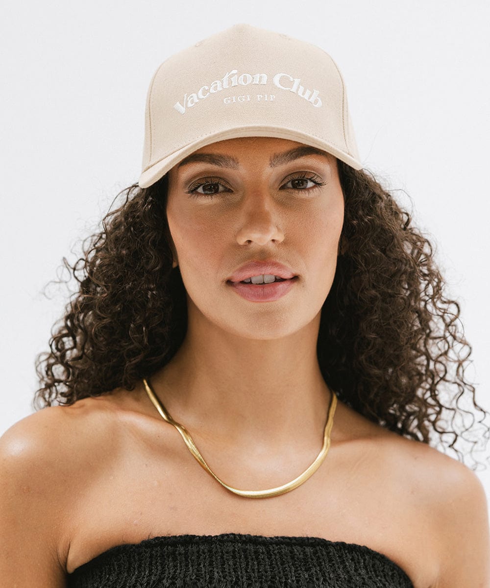 Woman wearing a tan cap with 'Vacation Club' text and a gold chain against a plain background #color_tan