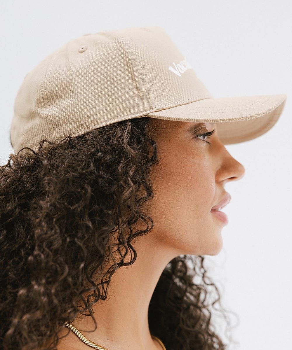 Woman wearing a tan cap with 'Vacation Club' text, facing sideways against a plain background #color_tan