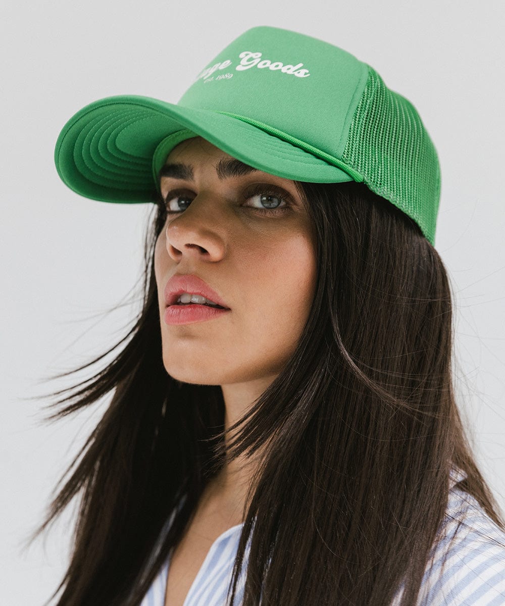 Woman wearing a vintage green colored trucker hat with 'Vintage Goods' text looking sideways against a plain background #color_vintage green