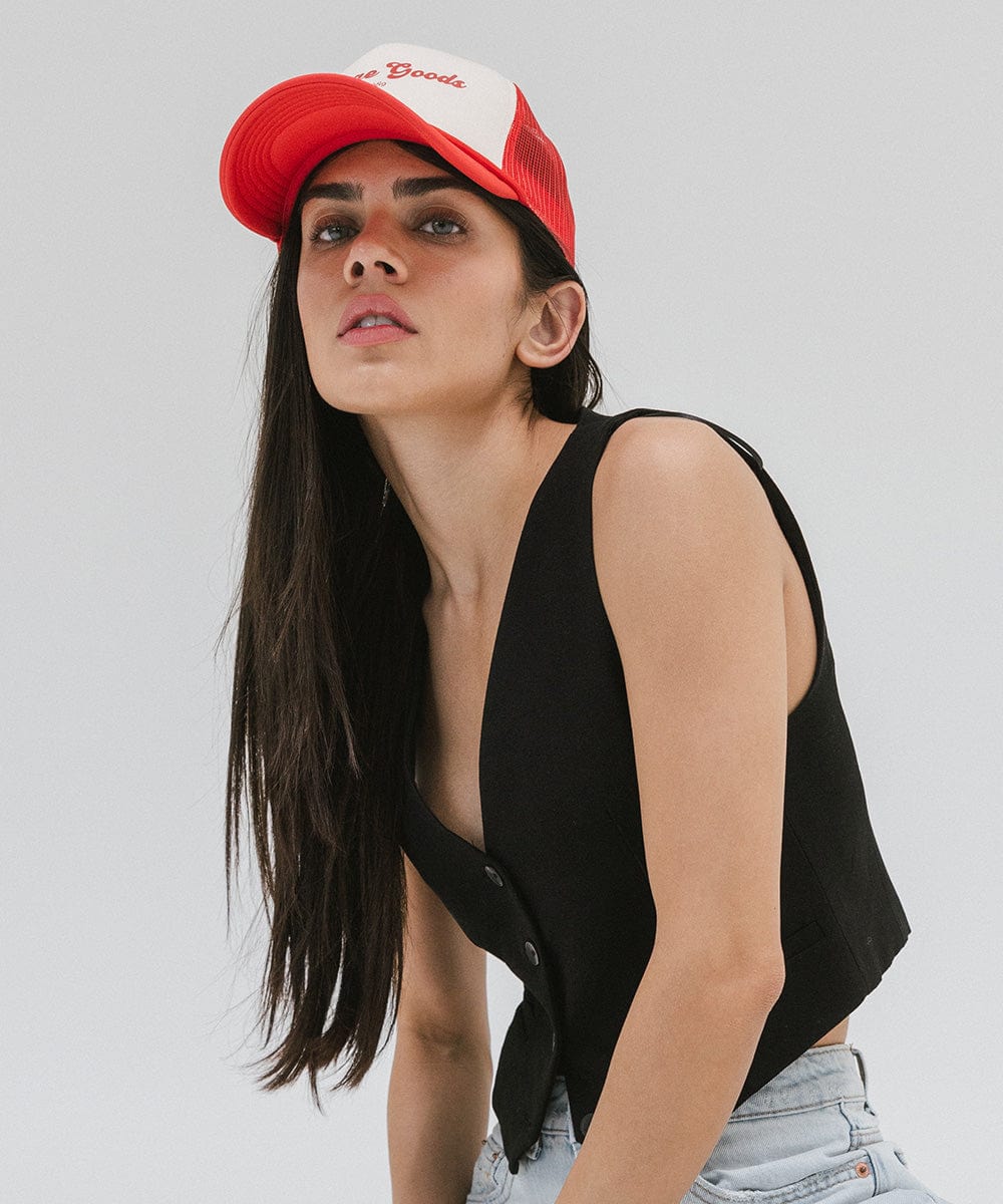 Woman wearing a cream and vintage red colored trucker hat with 'Vintage Goods' text and a black top, posing against a plain background #color_cream-vintage red