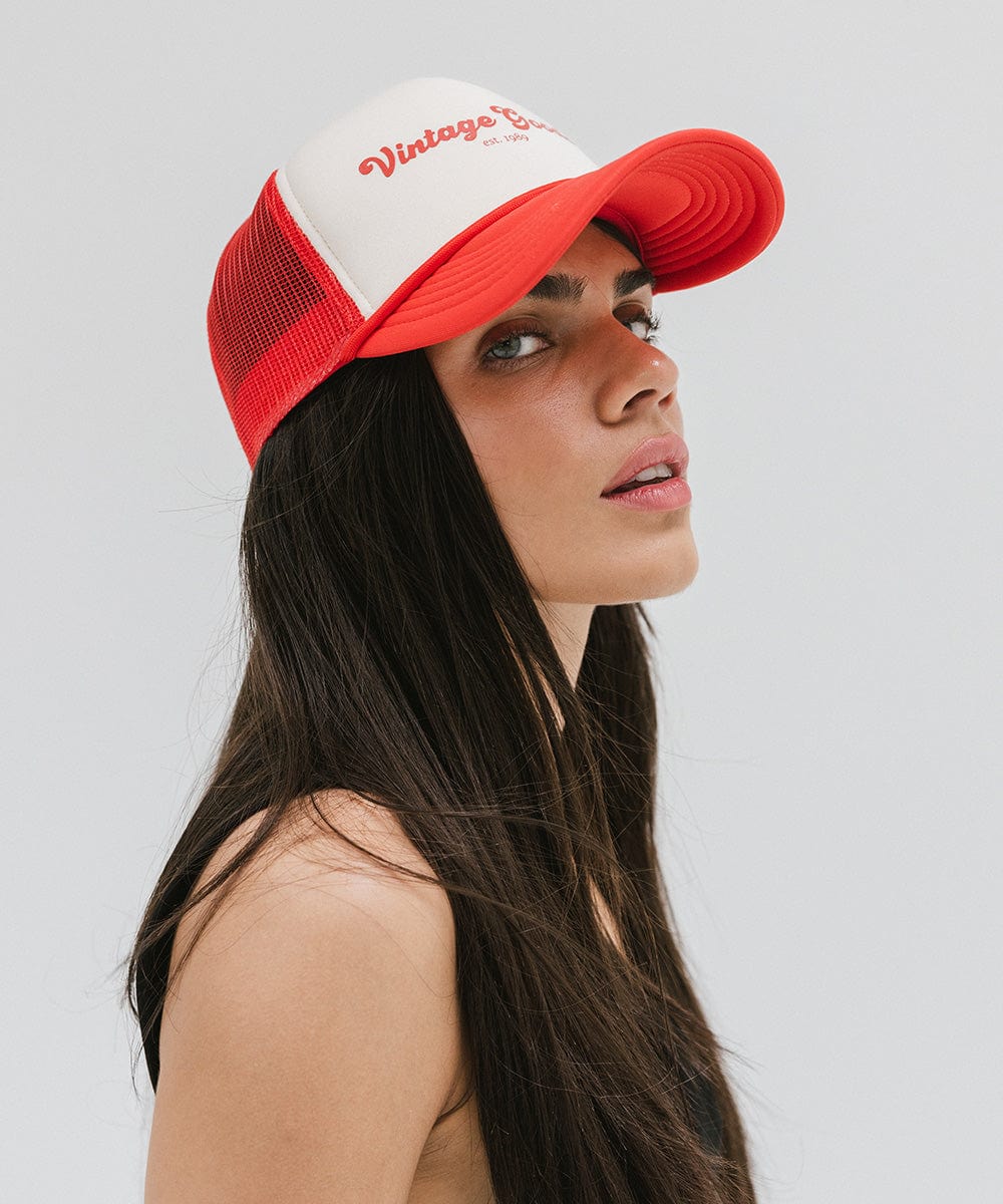 Woman wearing a cream and vintage red colored trucker hat with 'Vintage Goods' text against a plain background #color_cream-vintage red
