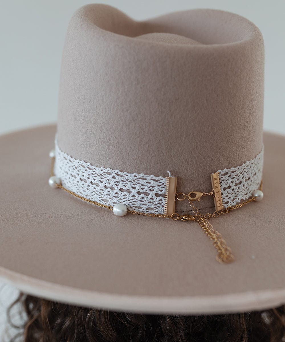 Close up image of a cream hat with a white lace band and a gold chain with beads against a plain background #color_white