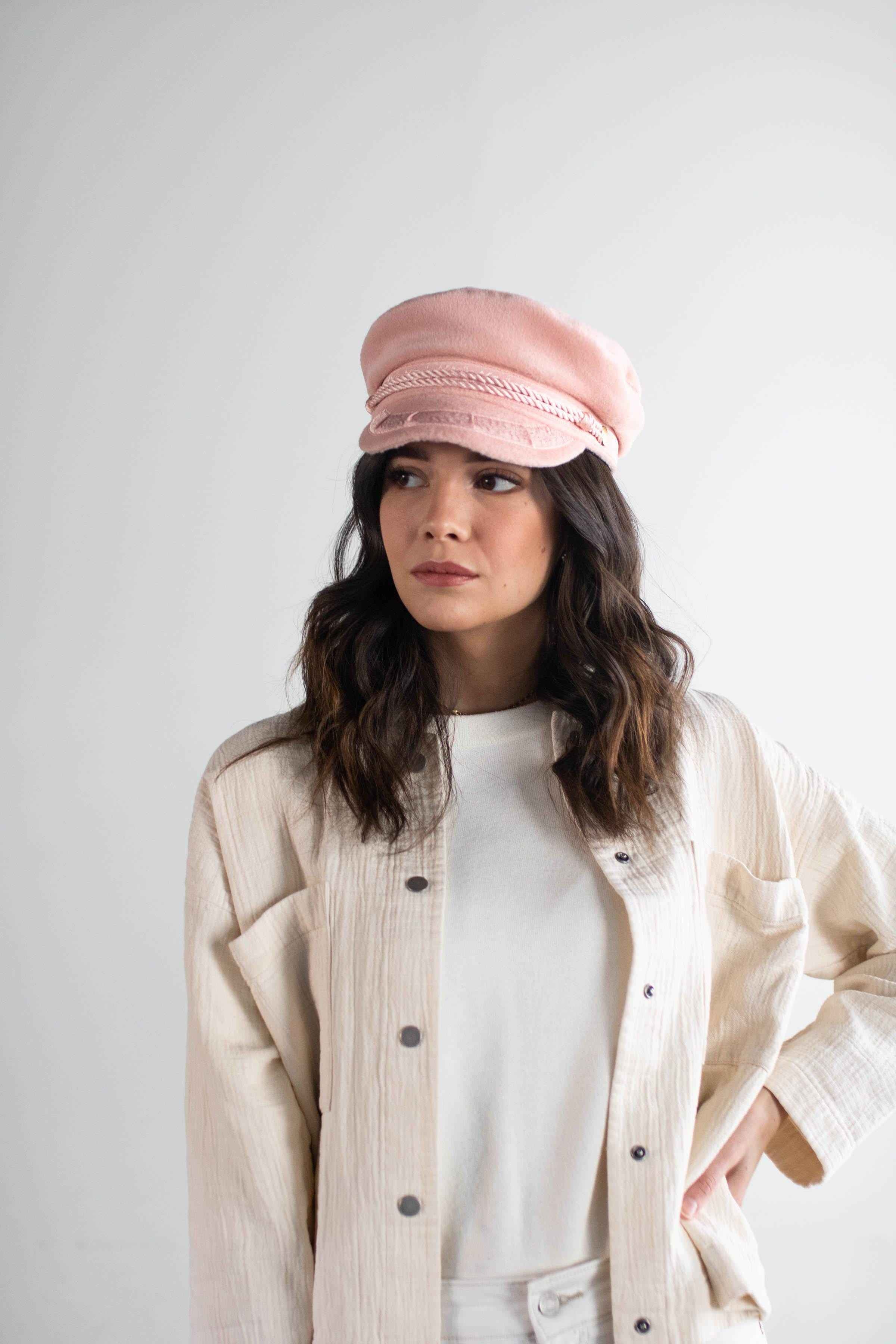 Woman wearing a blush colored lieutenant cap and a white t-shirt with a cream jacket against a plain background #color_blush