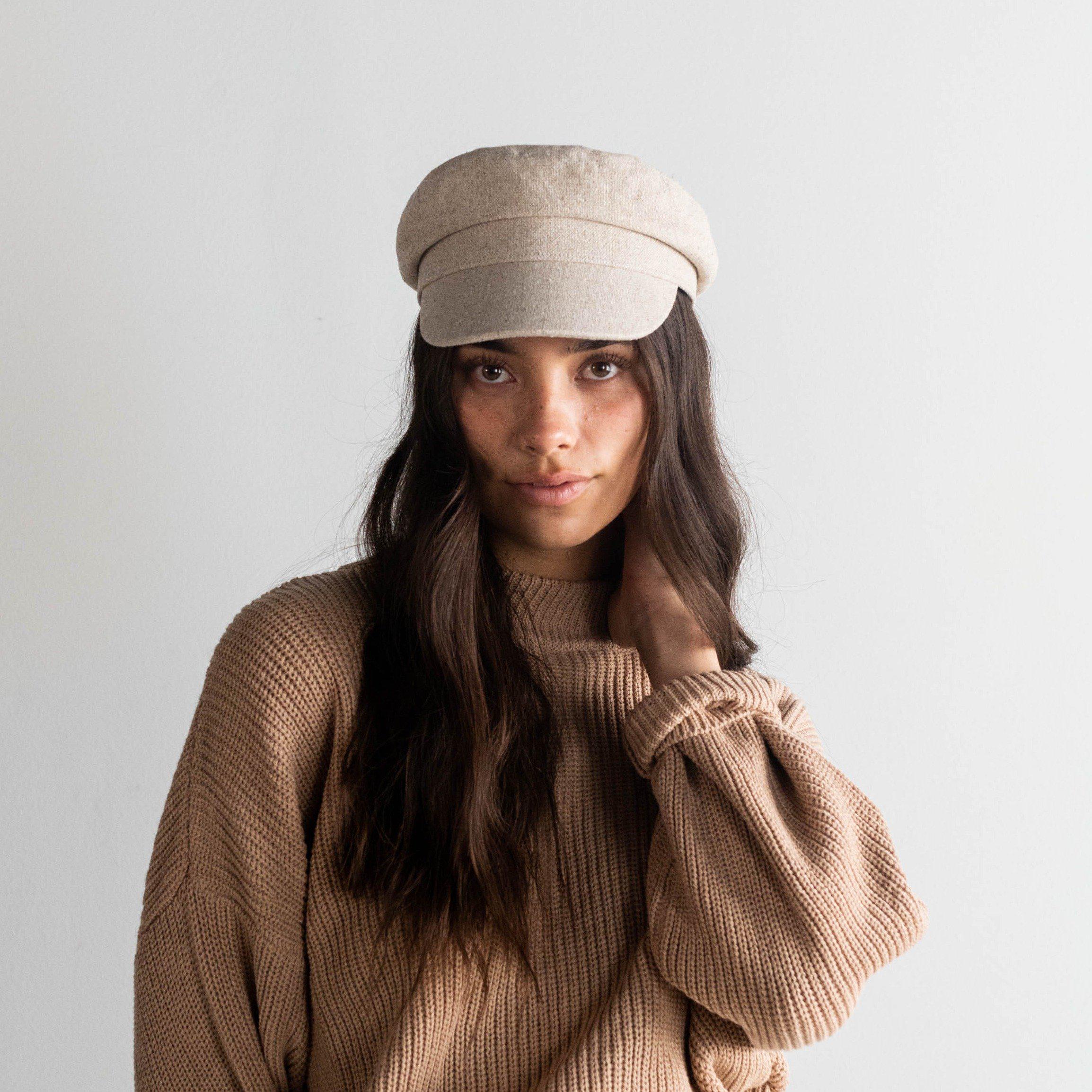 Woman wearing a linen colored cap and a brown sweater against a plain background #color_linen