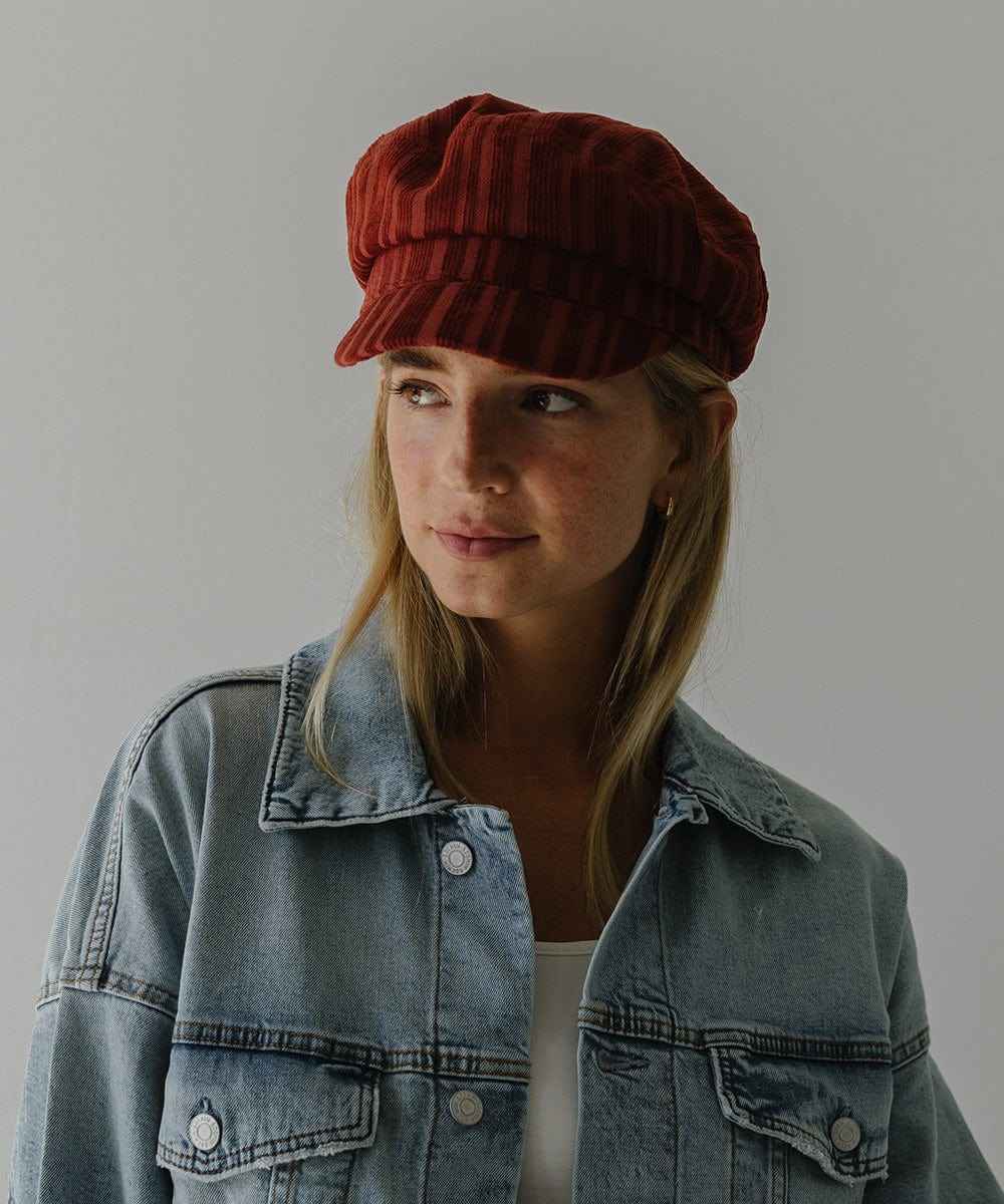Woman wearing a crimson red colored striped cap and a denim shirt against a plain background #color_crimson red