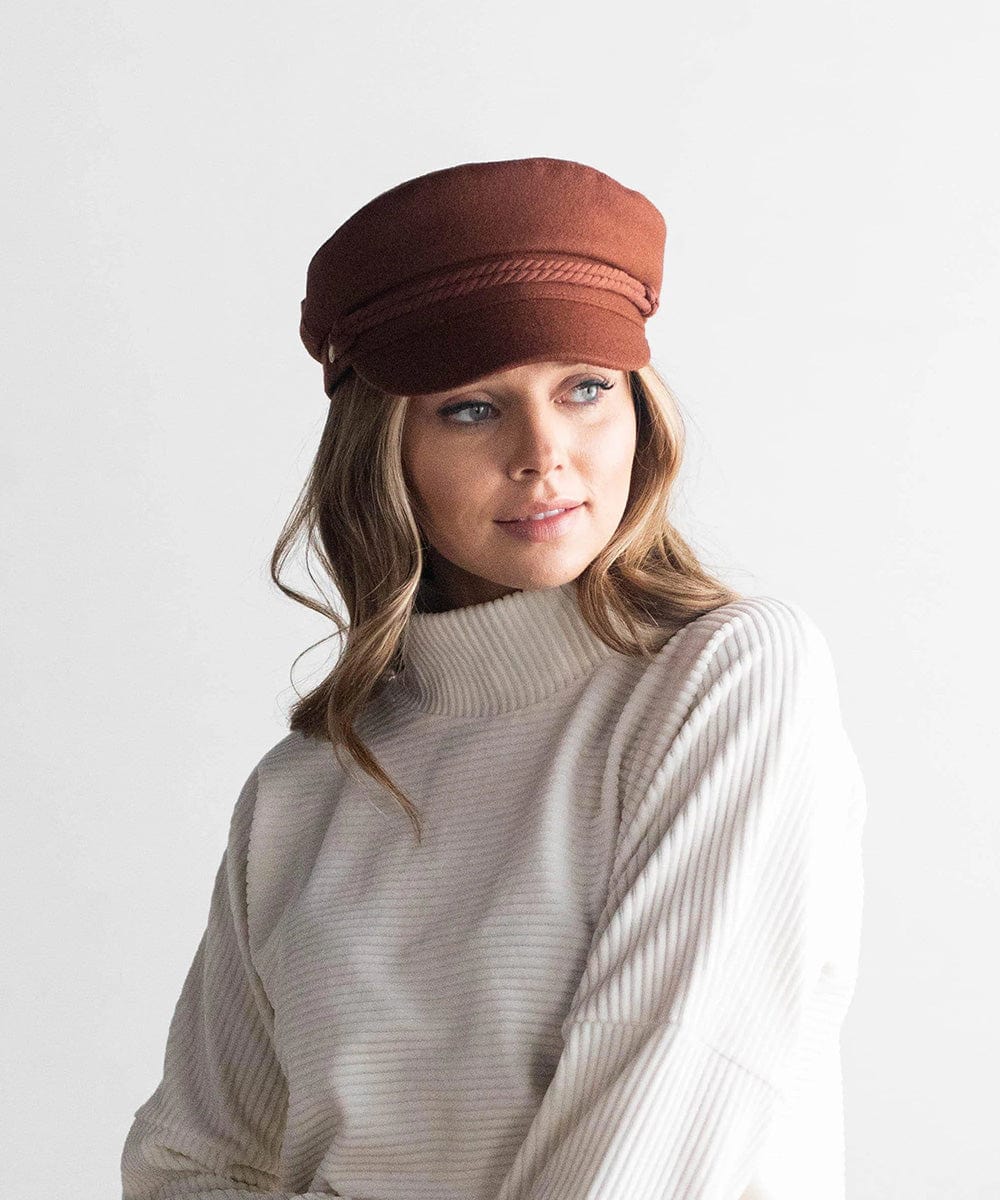 Woman wearing a chocolate brown colored fisherman cap with a rope detail and a white sweater against a plain background #color_chocolate brown