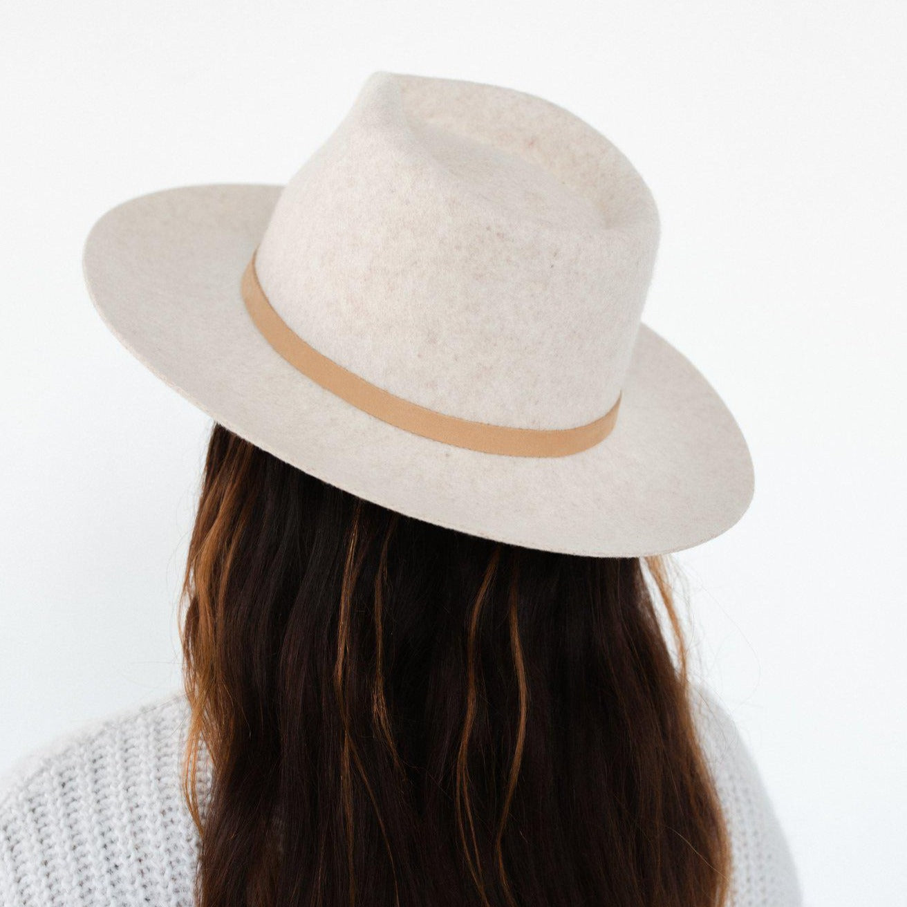 Woman wearing a white hat with a nude thin leather band, facing behind against a plain background #color_nude
