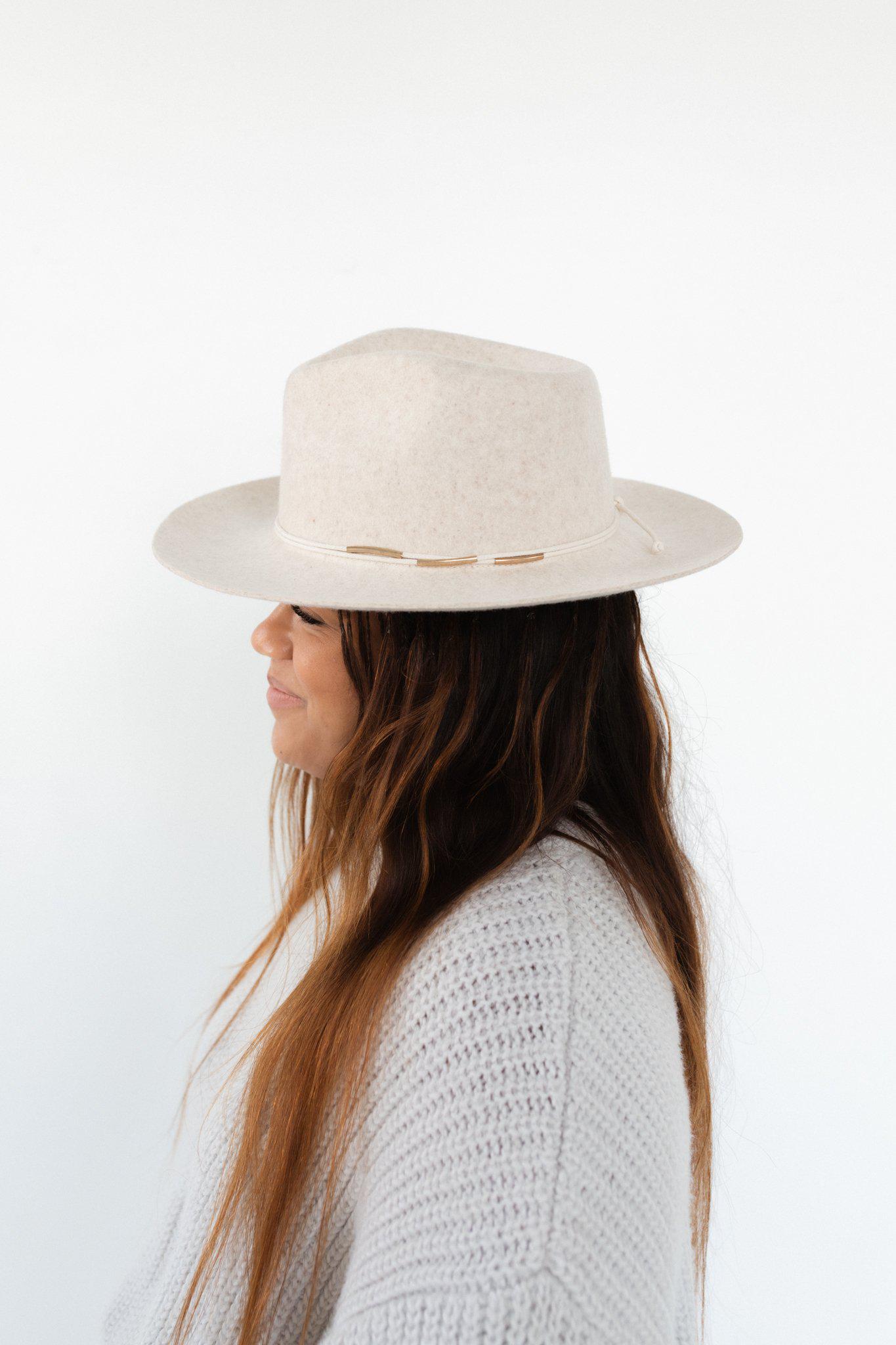 Woman wearing a white hat with a cream rope band with beads and a white sweater, facing sideways against a plain background #color_cream