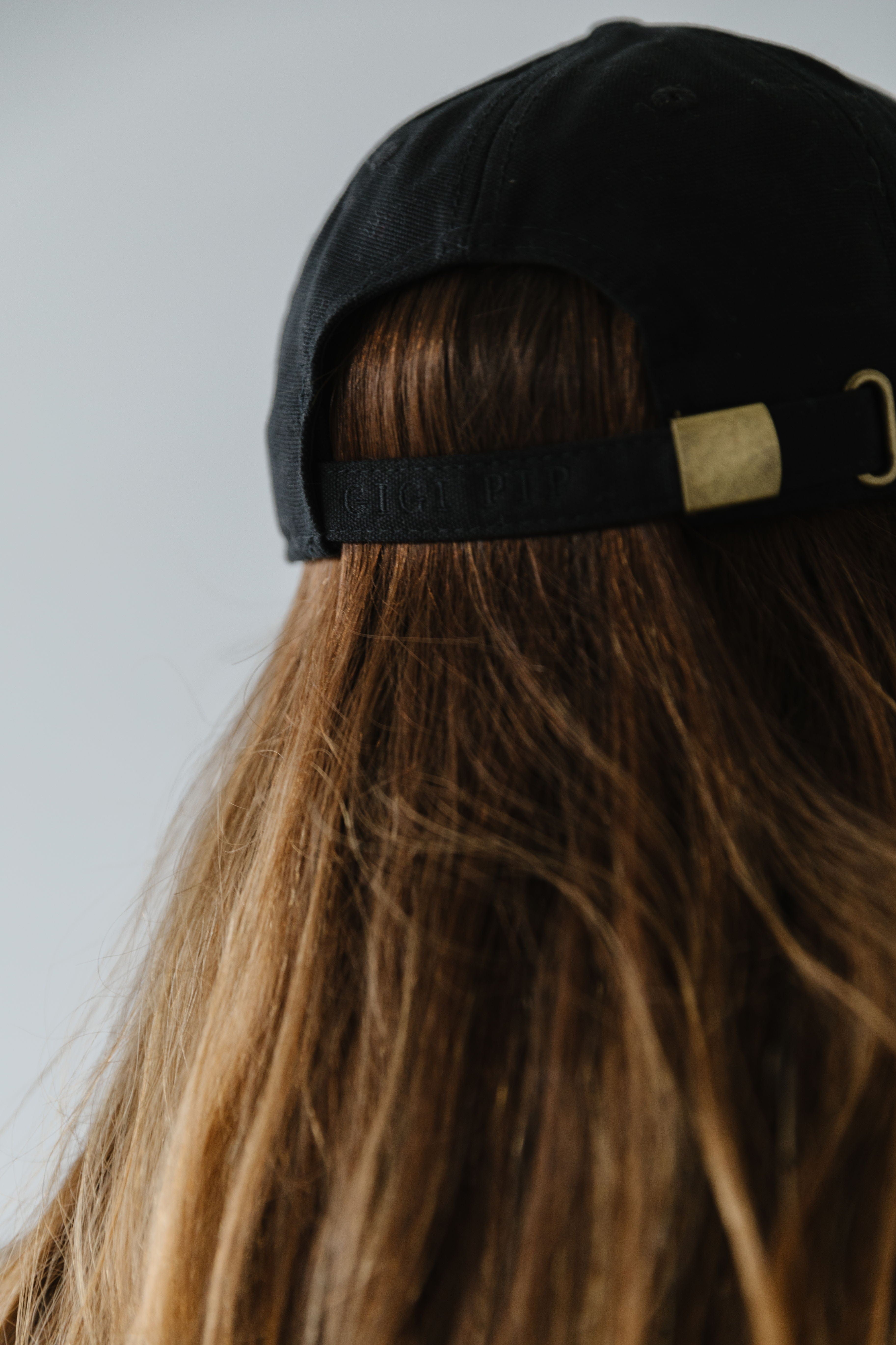 Woman wearing a black ball cap facing behind against a plain background #color_black